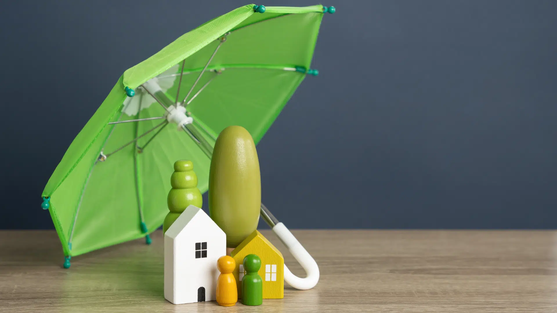 Arbre, maison et personnes en figurine sous un grand parapluie vert